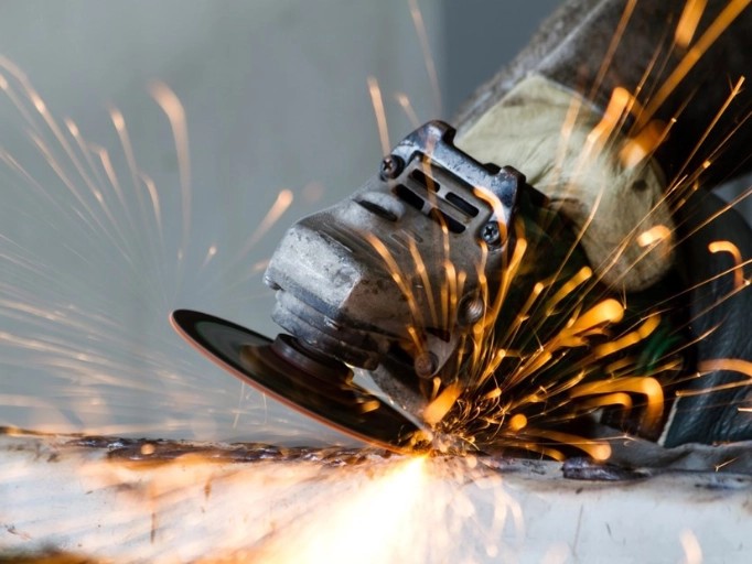 Mechanic using a cordless angle grinder to remove rust from a car chassis in an auto repair shop