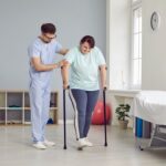 A caregiver assisting a senior patient with walking exercises at home, emphasizing fall prevention in home health care.